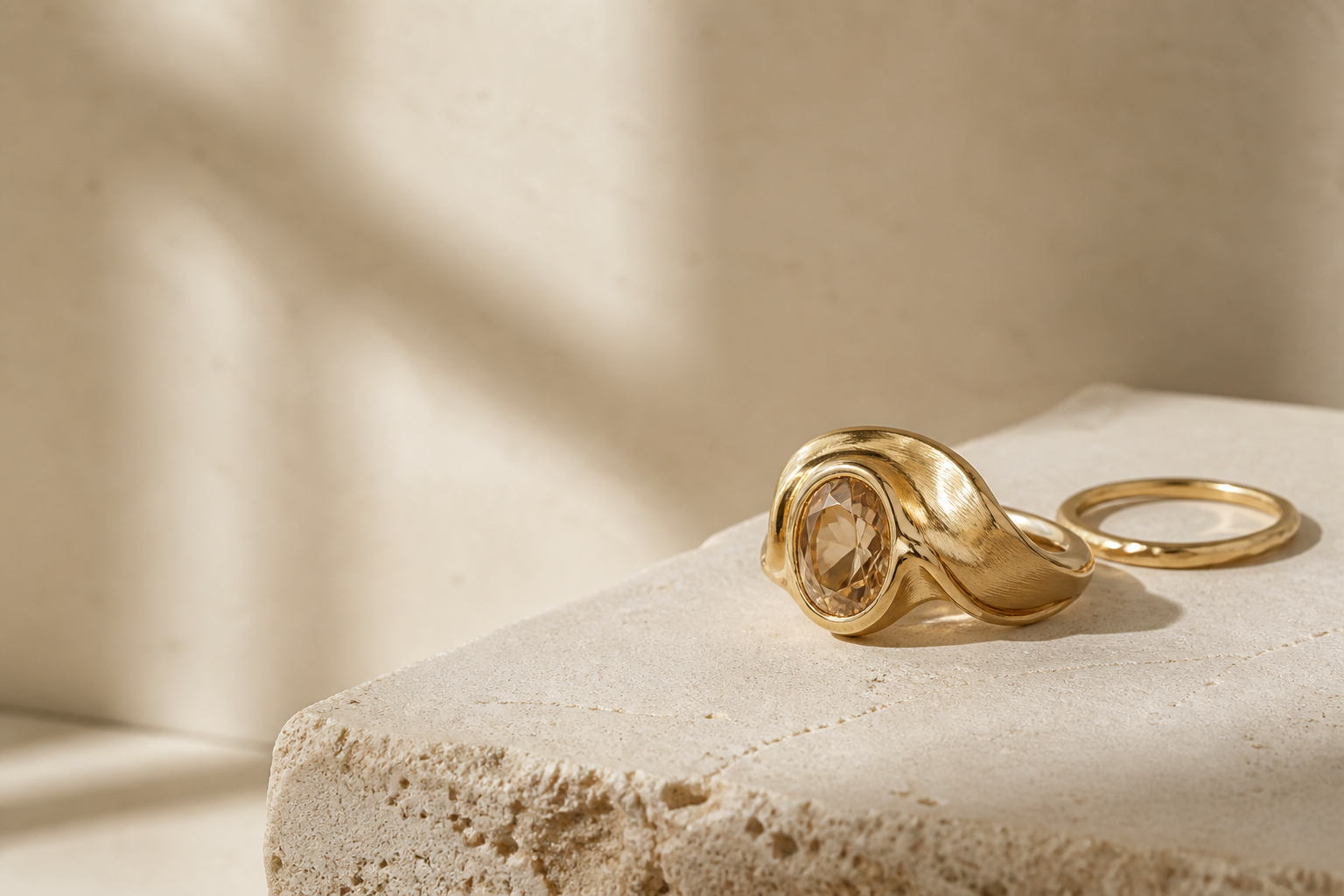 Sculptural gold rings resting on warm limestone